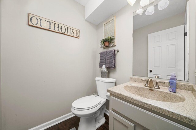 half bathroom featuring vanity, baseboards, toilet, and wood finished floors