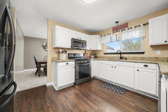 kitchen with dark wood finished floors, a sink, light stone counters, stainless steel appliances, and white cabinetry