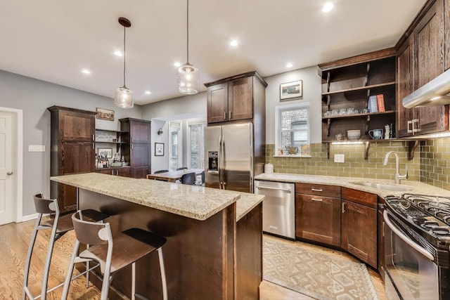 kitchen featuring dark brown cabinetry, appliances with stainless steel finishes, light stone counters, a sink, and light wood finished floors
