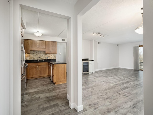 kitchen featuring wood finished floors, dark countertops, beverage cooler, tasteful backsplash, and a sink