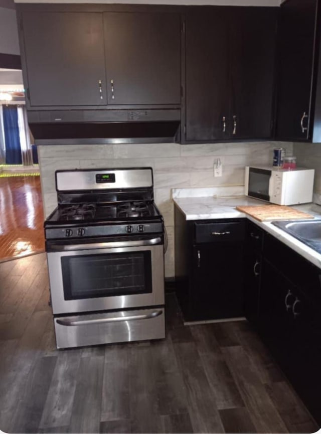 kitchen featuring light countertops, dark wood finished floors, white microwave, and gas range