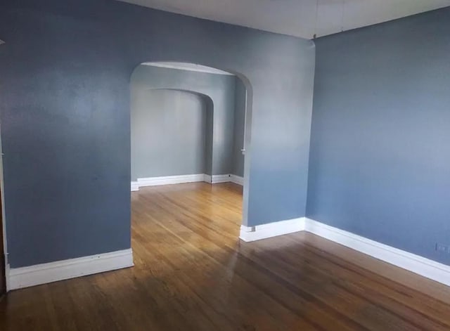 unfurnished room with arched walkways, baseboards, and wood finished floors
