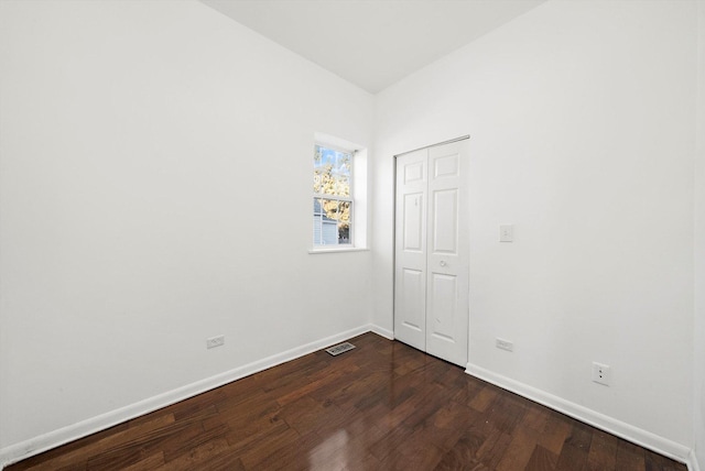 spare room featuring baseboards, dark wood finished floors, and visible vents