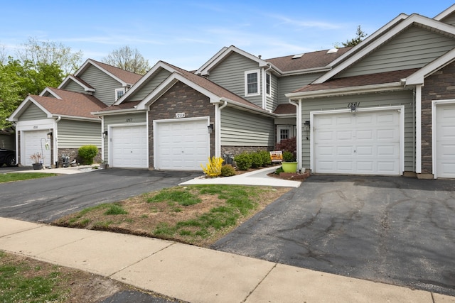 townhome / multi-family property with roof with shingles, driveway, and stone siding