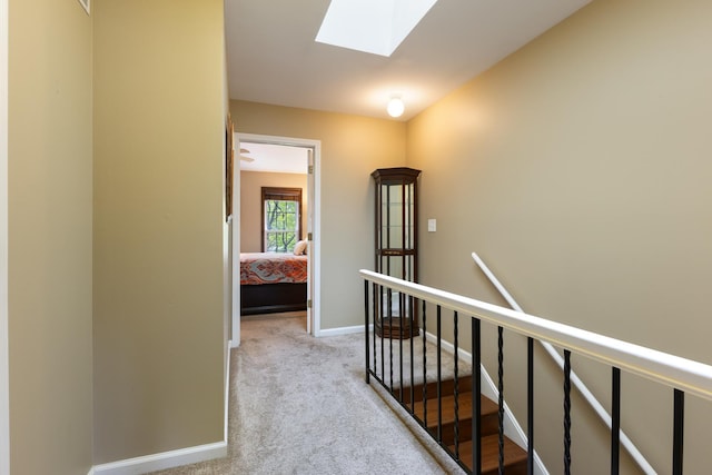 hall featuring a skylight, carpet floors, baseboards, and an upstairs landing