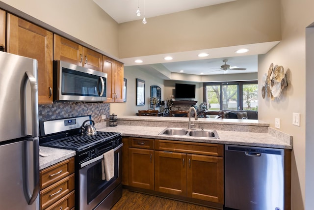 kitchen featuring appliances with stainless steel finishes, light stone counters, a sink, a peninsula, and open floor plan