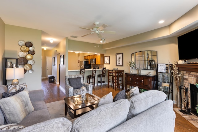 living area featuring visible vents, ceiling fan, dark wood-style floors, and a fireplace