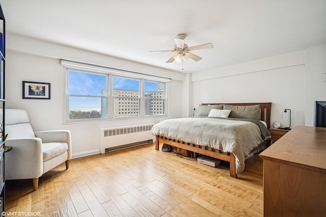 bedroom featuring baseboards, ceiling fan, radiator heating unit, and light wood-type flooring