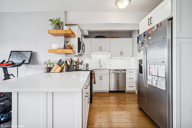 kitchen featuring backsplash, open shelves, a sink, stainless steel appliances, and white cabinetry