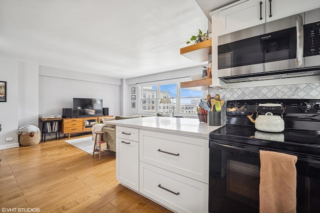 kitchen with black electric range, white cabinets, stainless steel microwave, and light wood-type flooring