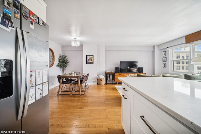 kitchen with stainless steel fridge, open floor plan, light wood-style flooring, and white cabinetry