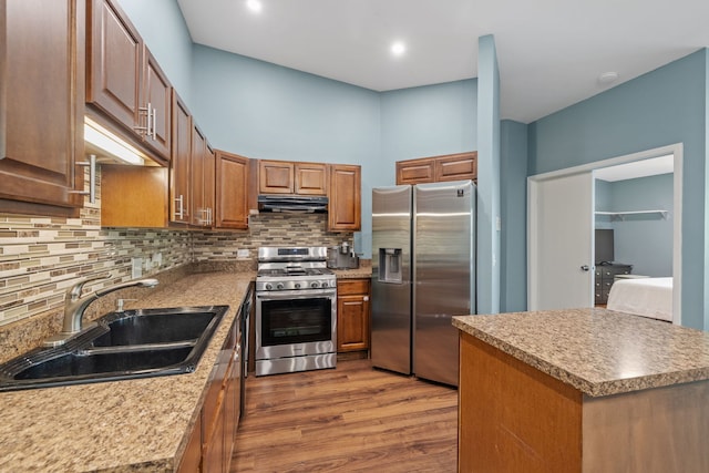 kitchen with appliances with stainless steel finishes, a sink, decorative backsplash, under cabinet range hood, and dark wood-style floors