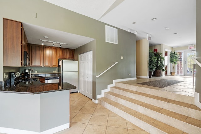 kitchen with appliances with stainless steel finishes, a sink, dark stone counters, light tile patterned floors, and visible vents
