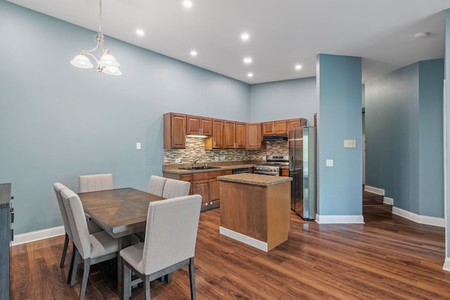 kitchen featuring brown cabinetry, a kitchen island, a sink, under cabinet range hood, and stainless steel appliances