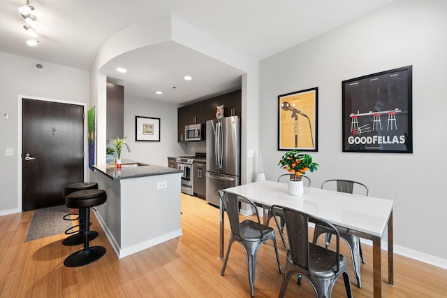 kitchen with light wood-style flooring, a peninsula, dark countertops, and stainless steel appliances