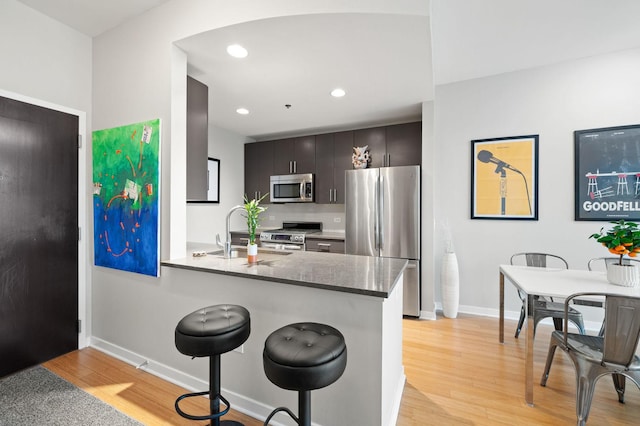kitchen featuring appliances with stainless steel finishes, a sink, a kitchen breakfast bar, light wood-style flooring, and baseboards