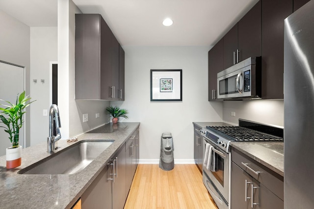 kitchen featuring appliances with stainless steel finishes, a sink, light wood-style floors, recessed lighting, and baseboards