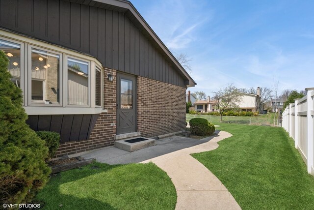 view of side of property featuring fence, board and batten siding, a yard, and brick siding
