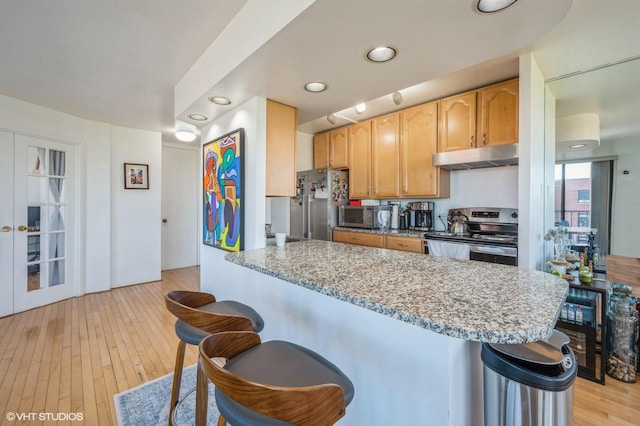 kitchen with a breakfast bar, stainless steel appliances, light stone countertops, and under cabinet range hood