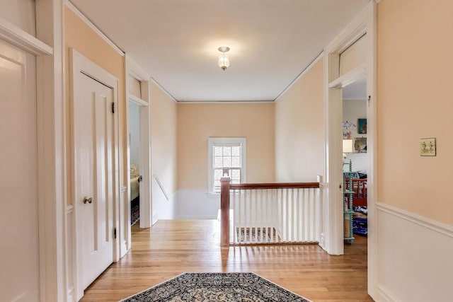 corridor with an upstairs landing, wood finished floors, and ornamental molding