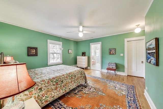 bedroom with wood finished floors, ornamental molding, ensuite bathroom, a ceiling fan, and baseboards