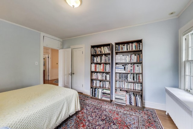 bedroom featuring radiator heating unit, wood finished floors, ornamental molding, and baseboards