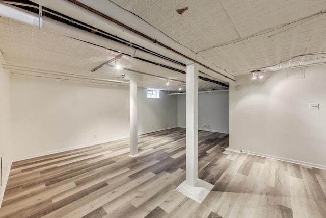 basement featuring rail lighting, wood finished floors, and baseboards