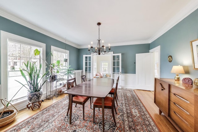 dining space featuring a chandelier, light wood-type flooring, crown molding, and a wainscoted wall