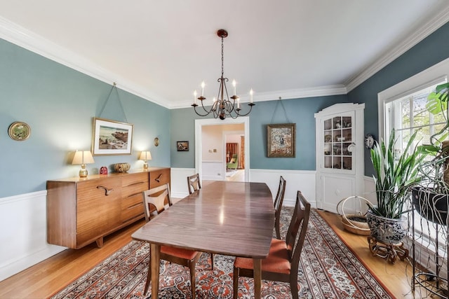 dining area with a chandelier, wood finished floors, a wainscoted wall, and ornamental molding