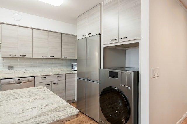 kitchen with washer / dryer, dishwasher, stainless steel refrigerator, wood finished floors, and light stone countertops