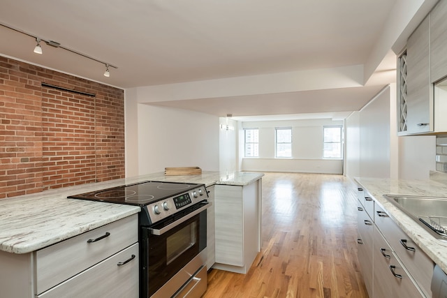 kitchen featuring stainless steel electric stove, brick wall, track lighting, open floor plan, and light wood finished floors