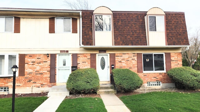 townhome / multi-family property with brick siding, a front lawn, roof with shingles, and mansard roof