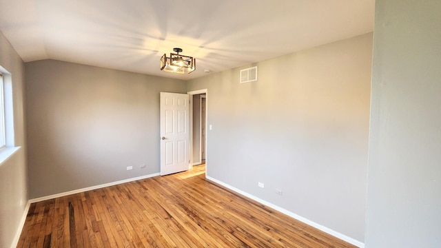 empty room with light wood-style floors, baseboards, lofted ceiling, and visible vents