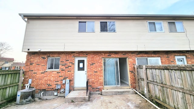 back of property with brick siding, central AC unit, fence, and entry steps