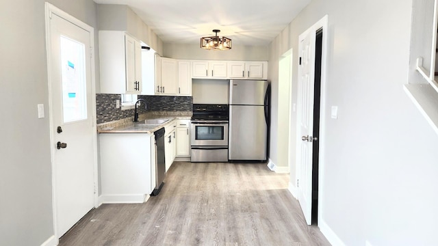 kitchen featuring white cabinets, appliances with stainless steel finishes, a sink, light wood finished floors, and a chandelier