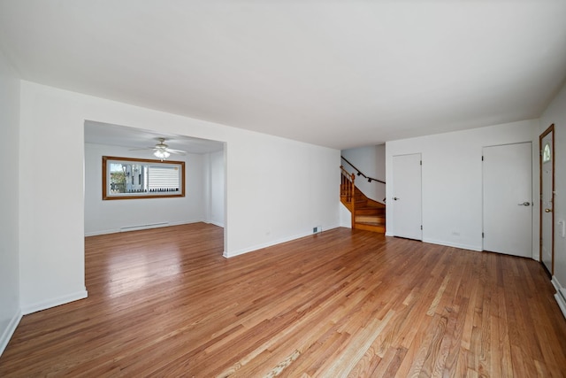 unfurnished living room with light wood-type flooring, baseboards, baseboard heating, and stairway