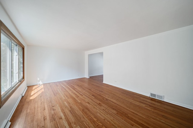 spare room featuring baseboards, a baseboard heating unit, wood finished floors, and visible vents