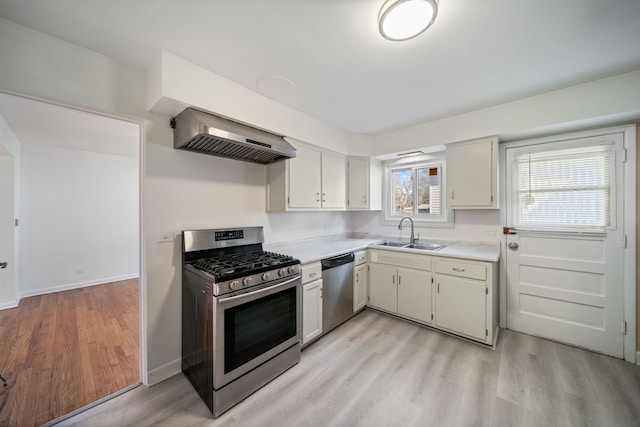 kitchen with appliances with stainless steel finishes, a sink, light countertops, light wood-style flooring, and range hood
