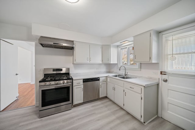 kitchen featuring wall chimney range hood, appliances with stainless steel finishes, a sink, light countertops, and light wood-type flooring