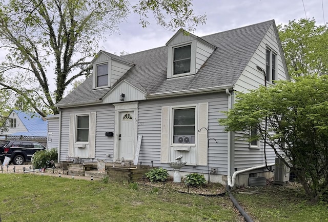new england style home with entry steps, a shingled roof, cooling unit, and a front lawn