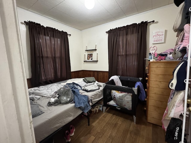 bedroom featuring wooden walls, crown molding, a wainscoted wall, and hardwood / wood-style floors