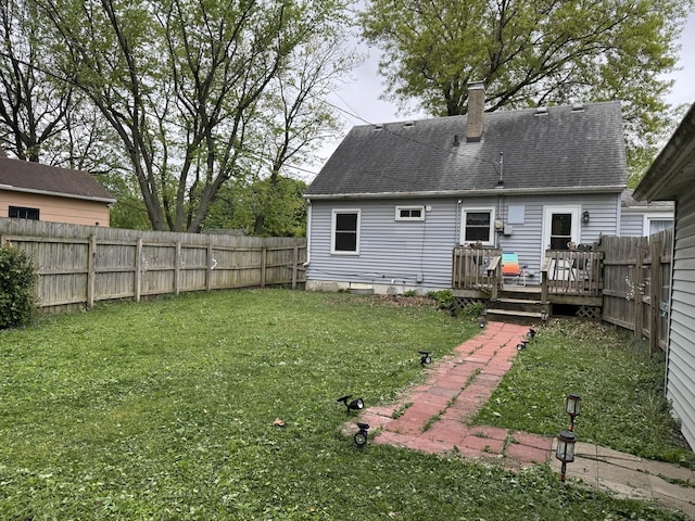 back of property with a chimney, a wooden deck, a fenced backyard, a yard, and a shingled roof