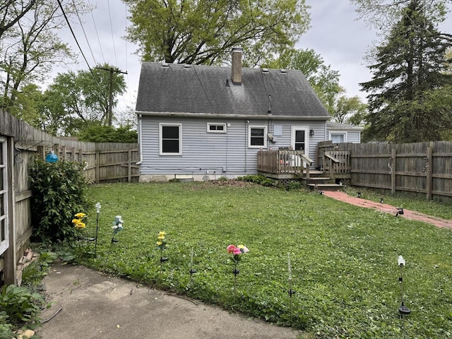 rear view of property featuring roof with shingles, a wooden deck, a fenced backyard, a chimney, and a lawn