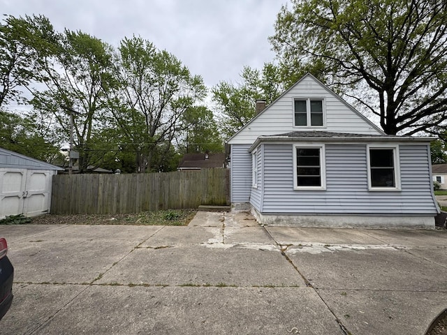view of side of home featuring a storage shed, fence, a chimney, and an outdoor structure