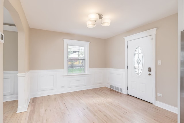 entryway featuring visible vents, light wood-style flooring, a wainscoted wall, and a chandelier