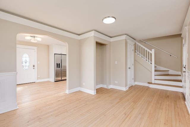 foyer entrance with baseboards, arched walkways, light wood finished floors, and stairway