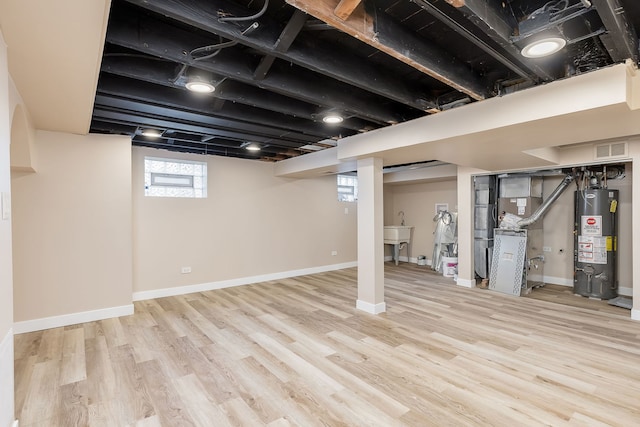 below grade area with gas water heater, visible vents, wood finished floors, baseboards, and heating unit
