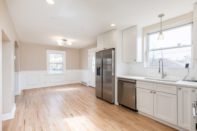 kitchen featuring a sink, a wainscoted wall, white cabinets, light wood finished floors, and stainless steel appliances