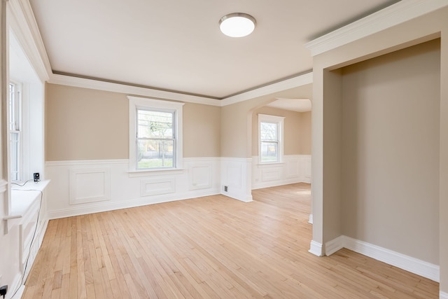 empty room with arched walkways, light wood-style flooring, and a wainscoted wall