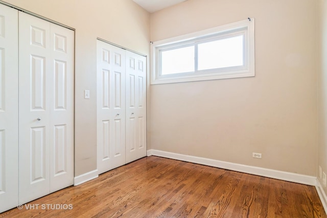 unfurnished bedroom with baseboards, light wood-style floors, and multiple closets